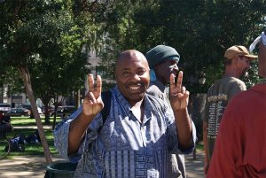an image of an African-American man in a blue shirt holding up double peace signs with his hands