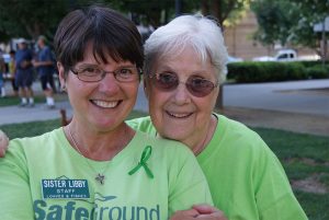 an image of two older women in green shirts standing together and smiling at an outdoor event